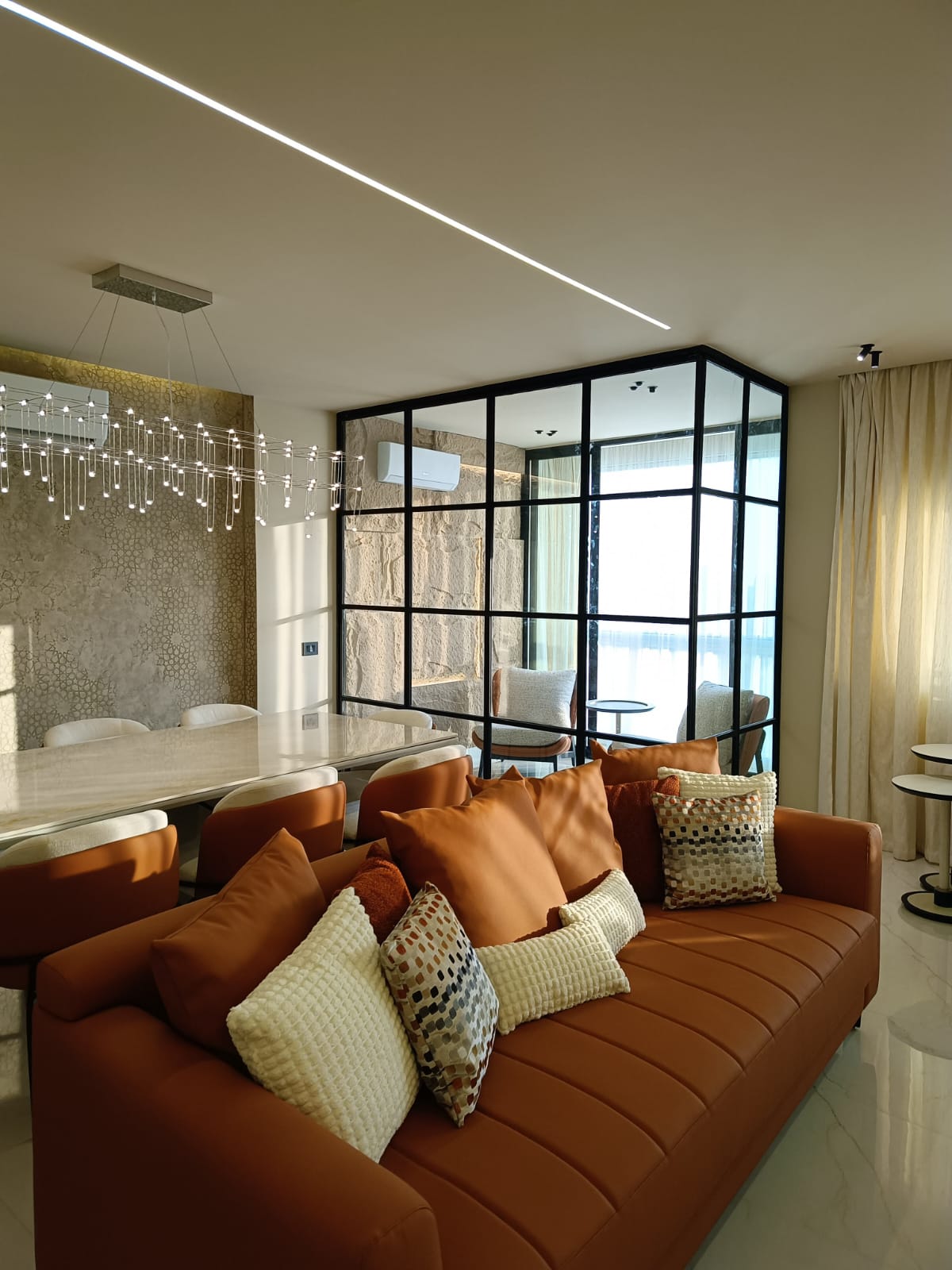 Living and dining space with terracotta sofa and steel-framed glass partition